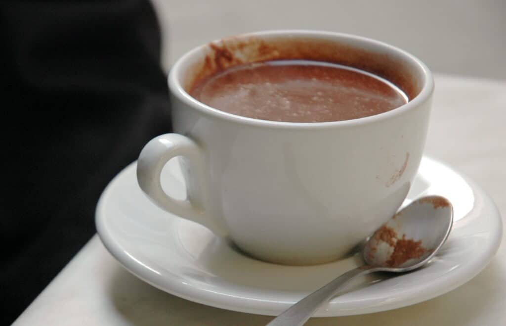 A white cup filled with thick Italian hot chocolate. A chocolate-covered silver spoon lies next to the cup on a white saucer.