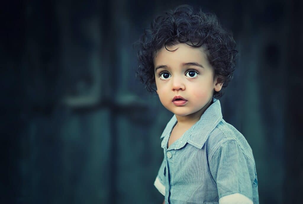 A curly-haired baby dressed in grey.