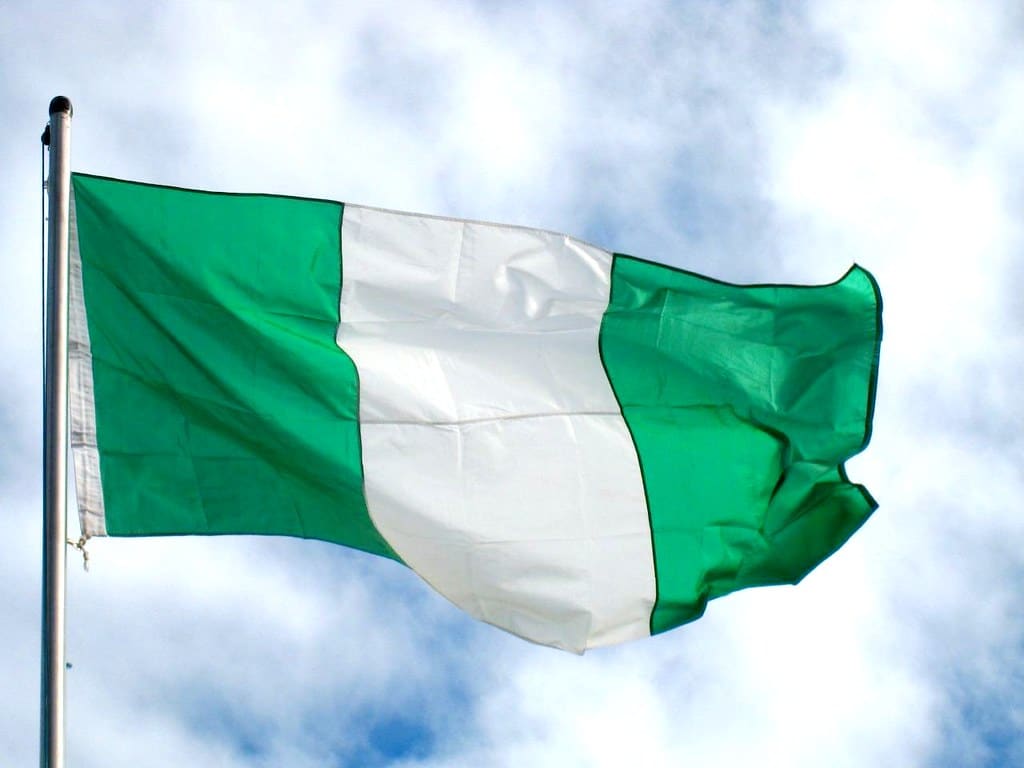 The Nigeria flag flying in the wind against a slightly cloudy sky.