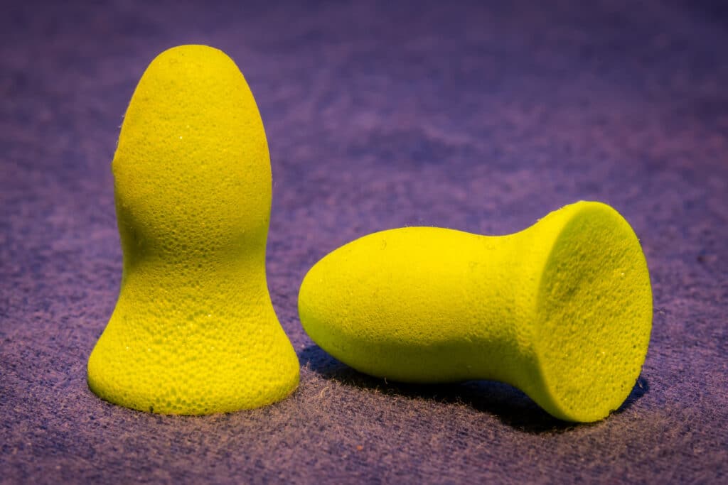 A pair of yellow ear plugs resting on a purple surface.