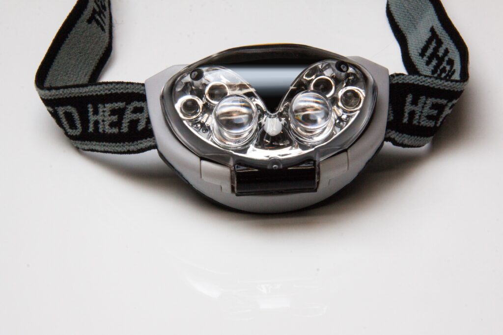 A grey and black headlamp and strap on a white surface. A headlamp is one of the most important travel essentials for hostel hopping.