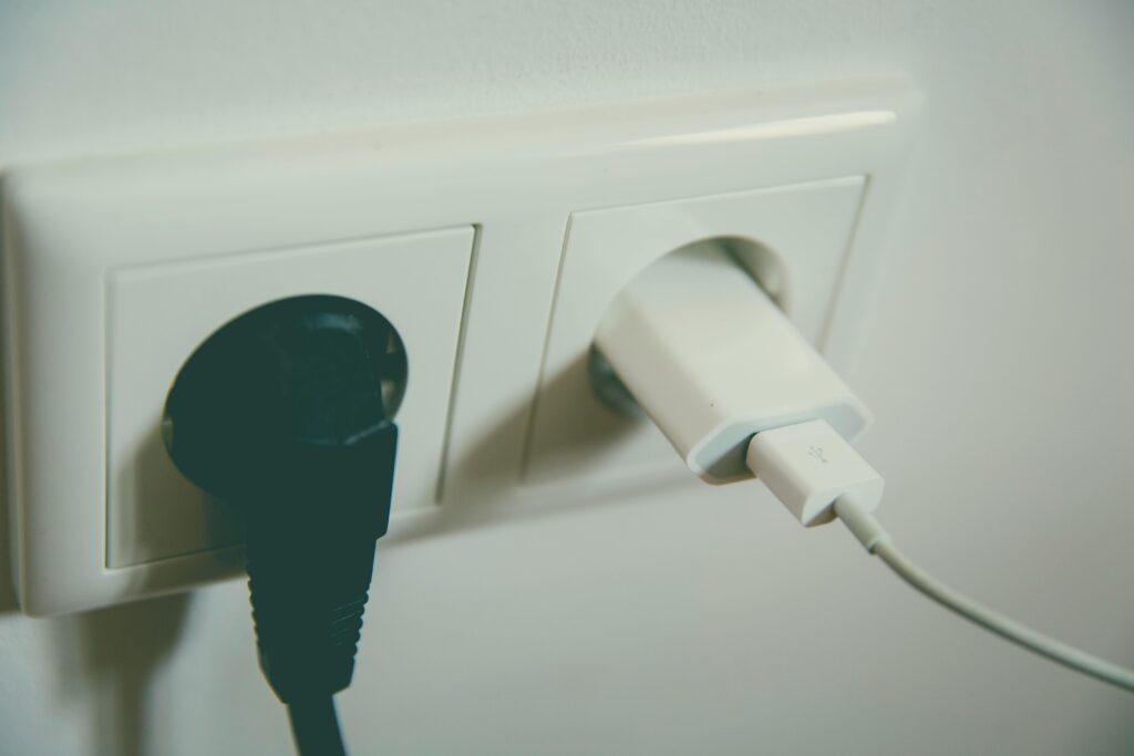 A blag plug (left) and a white travel adapter (right) in a power outlet in a wall.