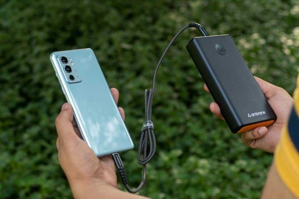 The hands of an anonymous person holding a phone (left) and a power bank (right).