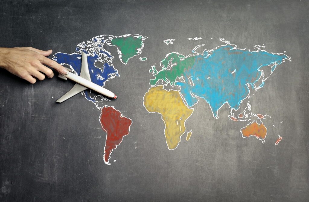 Top view of crop anonymous person holding toy airplane on colourful world map drawn on chalkboard.