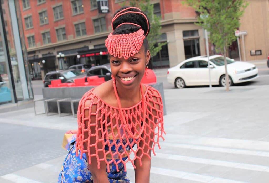 A beautiful Esan lady is dressed in traditional attire with an elaborately patterned bead blouse and a matching headset.