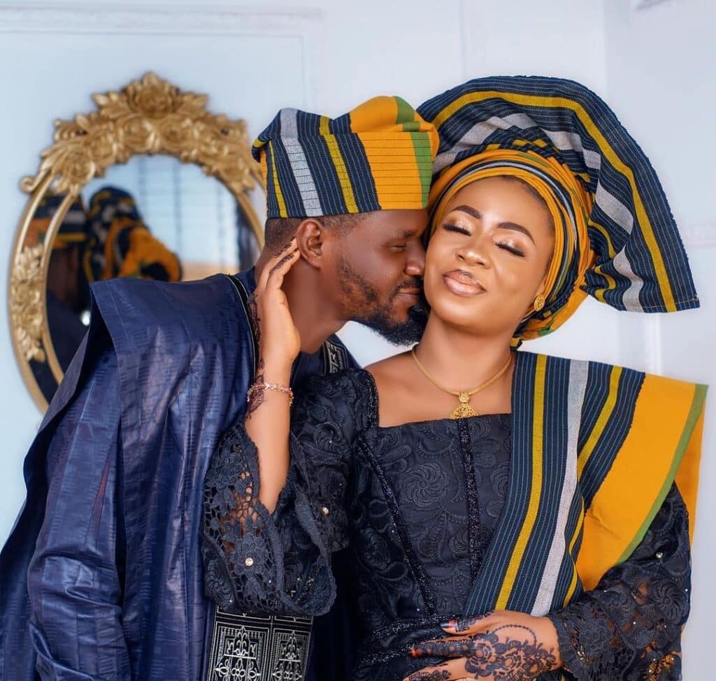 An Urhobo couple poses for a picture on their wedding day; the couple is dressed in traditional fabric, matching headpieces and general style.