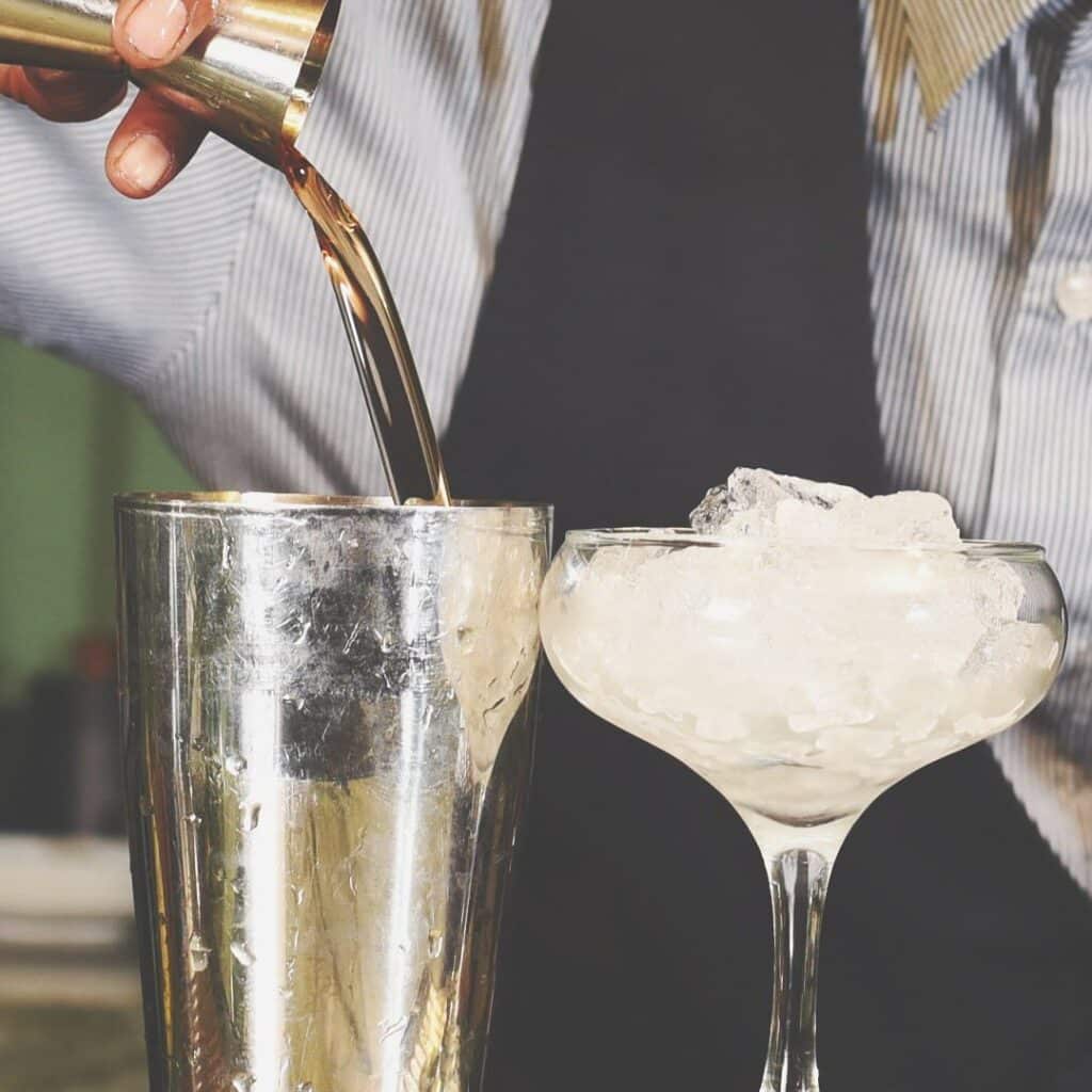 A bartender expertly pours a drink mix into a shaker, with a glass of ice ready beside it, creating a tantalising cocktail in preparation for patrons at one of the pubs in Lagos.