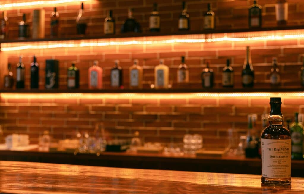 A whiskey bottle, prominently displayed on a counter, stands as a focal point amidst a blurred background of assorted beverages, evoking a sense of sophistication.