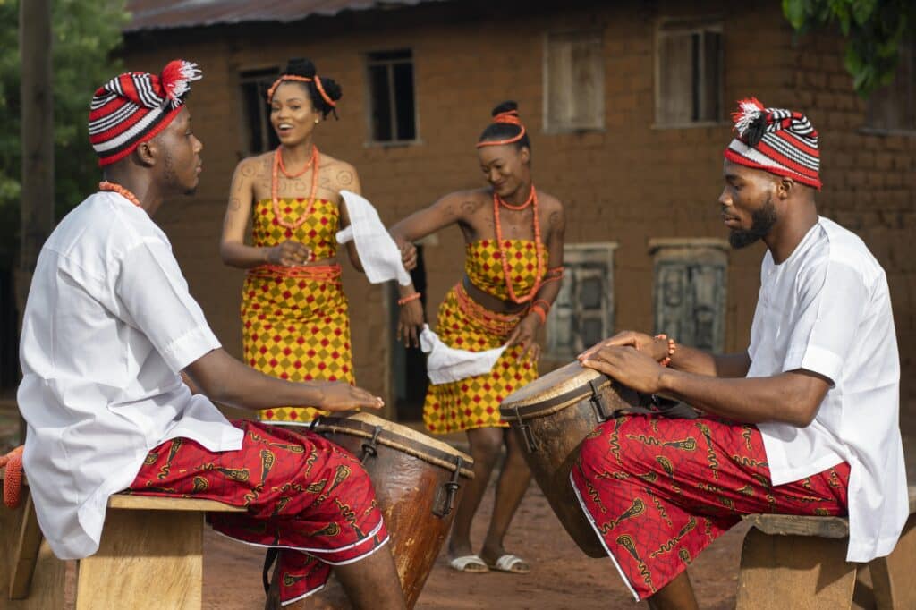 A group of Igbo tribe members adorned in cultural outfits and playing drums. 