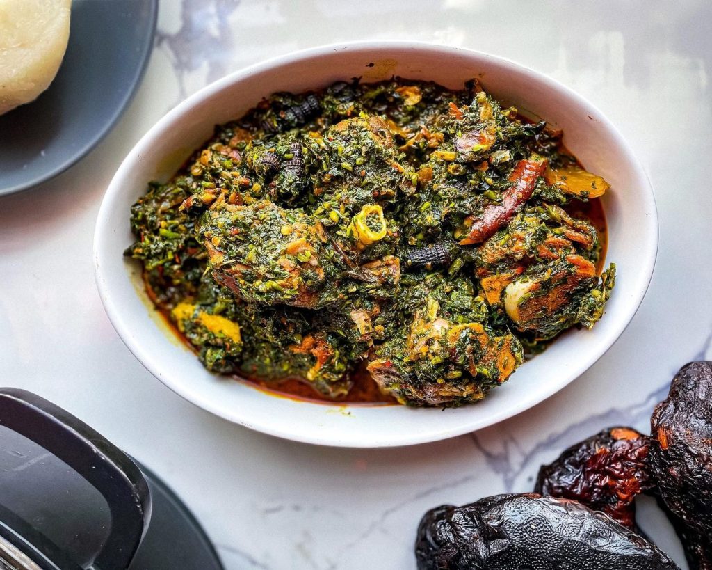 An enticing bowl of Afang Soup, a traditional Nigerian soup made with a rich, green leafy base, assorted meats, and flavorful spices, served with a side of fufu. 