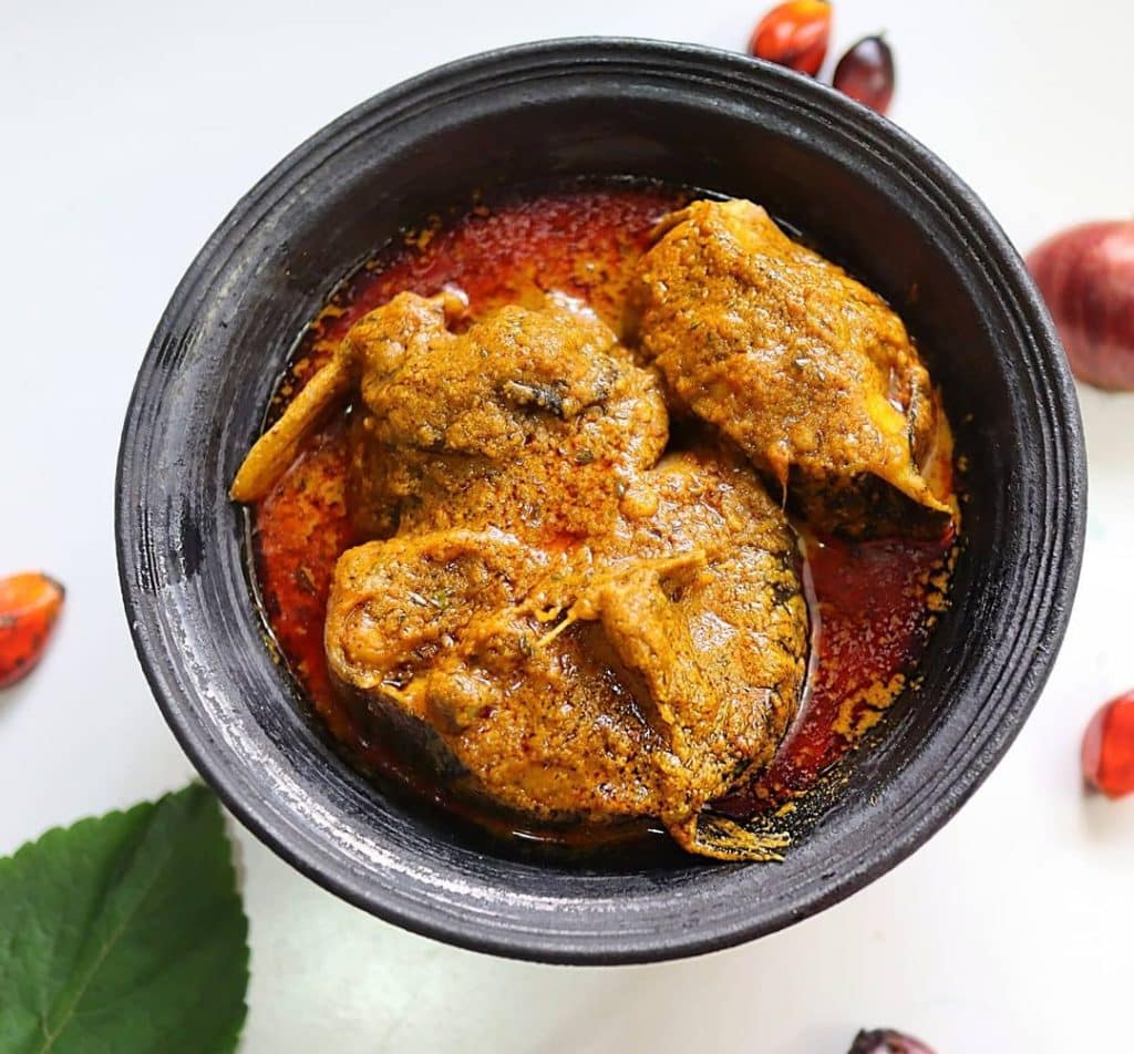 Steaming bowl of Banga Soup, a traditional Nigerian soup made from palm fruit extract, typically served with assorted meats and fish, accompanied by a side of fufu or rice.