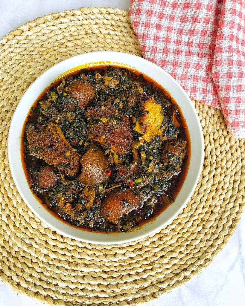 A bowl filled with vibrant green Efo-Riro Soup, a traditional Nigerian dish made with spinach, assorted meats, and flavorful spices, served with a side of fluffy white rice.