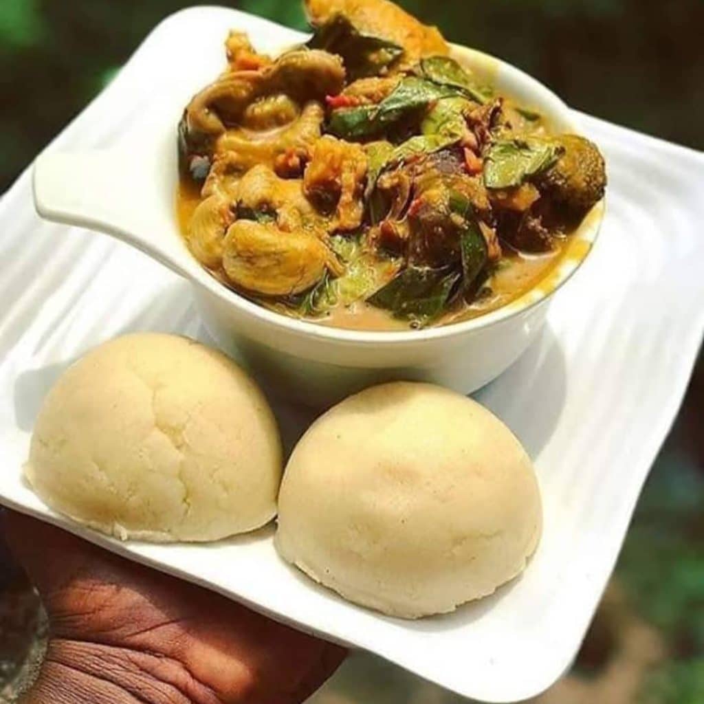 An appetizing bowl of Ora Soup, a traditional Nigerian delicacy, featuring  green vegetable leaves immersed in a rich, aromatic broth, garnished with assorted meats and spices.